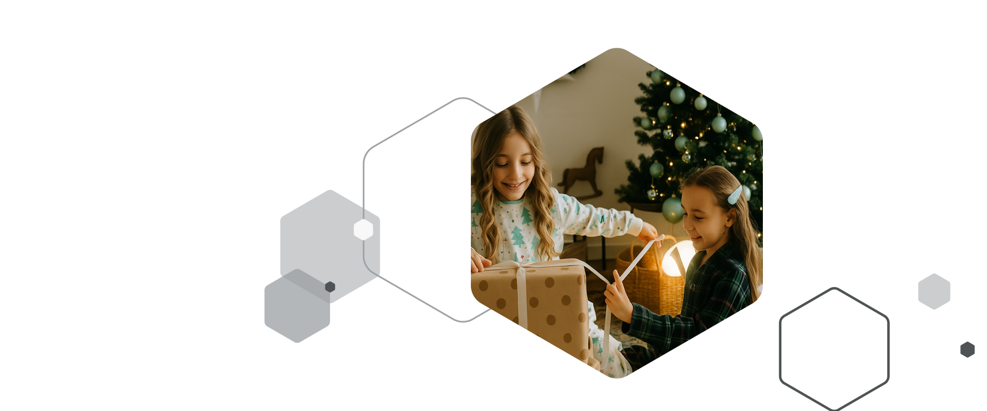 Zwei lächelnde Mädchen sitzen auf dem Boden vor einem beleuchteten Weihnachtsbaum und packen ein großes, mit braunem Punktepapier verpacktes Geschenk aus. Das ältere Mädchen (rechts, im Pyjama mit Tannenbaum-Muster) hält das Geschenk, während das jüngere Mädchen (links, im grün-karierten Pyjama) ein weißes Band abzieht.