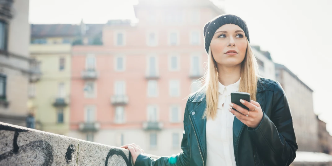 Una giovane donna con uno smartphone in mano in città: in questo caso le notifiche push con geofence possono rivelarsi molto utili