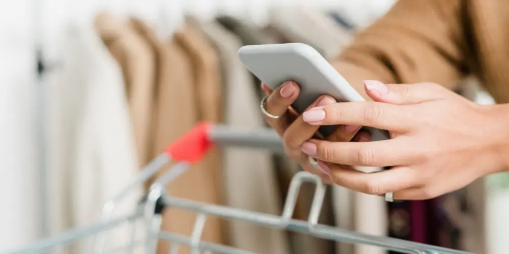 Woman uses her smartphone while pushing a shopping cart in a clothing store – digital customer engagement via the mobile-pocket app