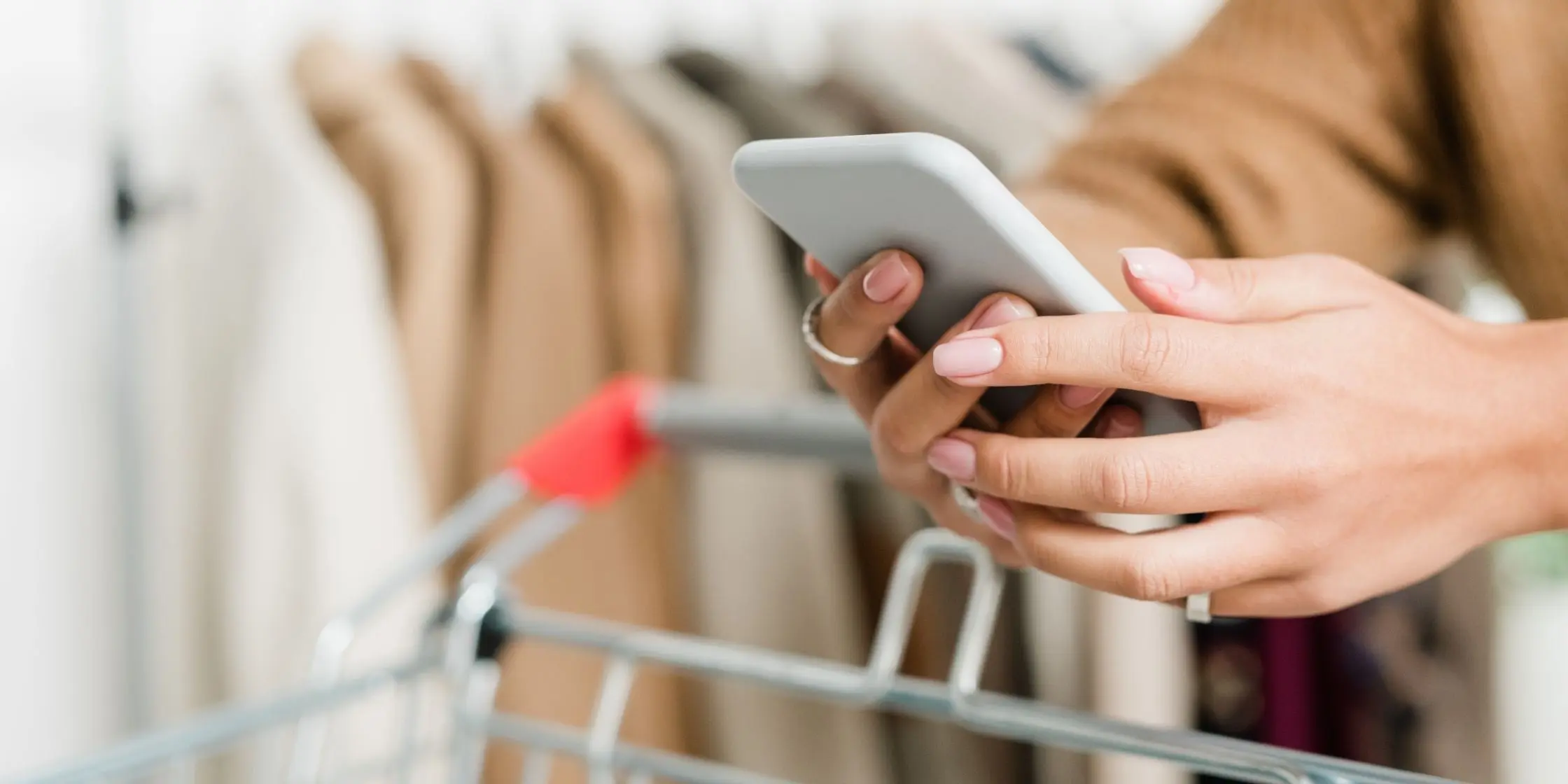 Woman uses her smartphone while pushing a shopping cart in a clothing store – digital customer engagement via the mobile-pocket app