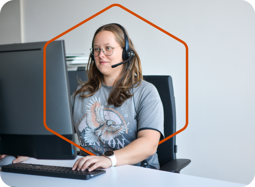 Frau mit Headset sitzt am Schreibtisch vor einem Bildschirm.